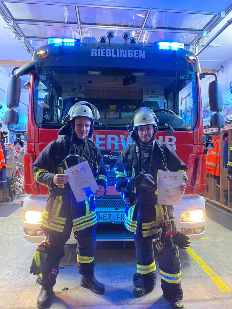 Zwei Feuerwehrleute stehen vor dem Rieblinger Feuerwehrauto und halten jeweils eine Urkunde in den Händen.